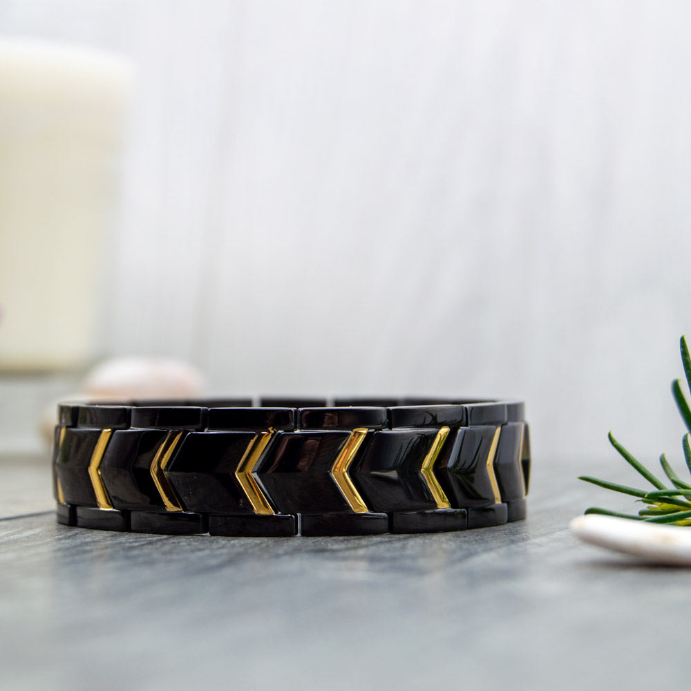 Mens Bracelets for Migraine - image shows a Black and gold coloured 4in1 Magnetic bracelet on a wooden surface