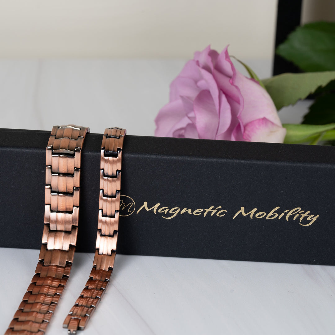 Ashe Copper Magnetic Bracelets - 9mm slim band and 15mm wide band - displayed draped over a Magnetic Mobility gift box with a pink rose in the background.