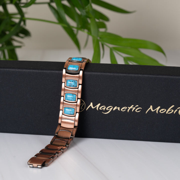 Asphodel Copper Magnetic Bracelet draped over a black Magnetic Mobility gift box, highlighting its geometric pattern and vibrant turquoise stones.
