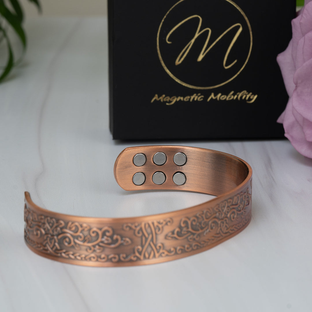 Close-up side view of the Campion Copper Bracelet, showing the six embedded magnets inside the open-backed bangle. The detailed floral design runs seamlessly along the bracelet.