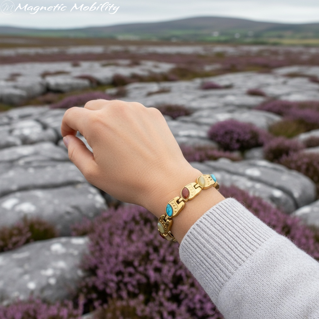 Hand wearing a gold magnetic bracelet with colorful stones against a blurred natural background