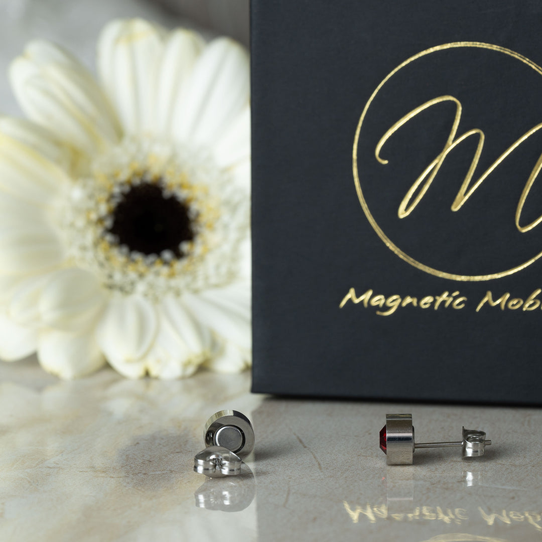 Side view of the July Birthstone magnetic earrings adorned with vibrant Swarovski Ruby crystals, set against a backdrop of a white flower and black gift box. These earrings exemplify the fiery beauty and elegance associated with July’s birthstone.