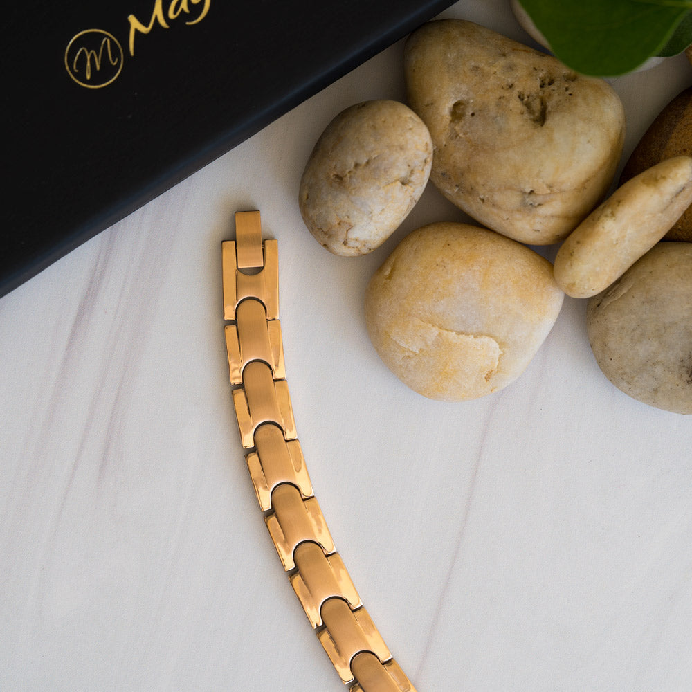 Top-down image of a Rowan Dawn men's bracelet, constructed from rose gold-toned stainless steel. The design, featuring interconnected links with a matte inlay and shiny outer stripe, provides a captivating pattern. The secure clasp merges flawlessly into the design. The bracelet serves as a chic accessory and is also promoted for relief from conditions like arthritis, back pain, and migraines.