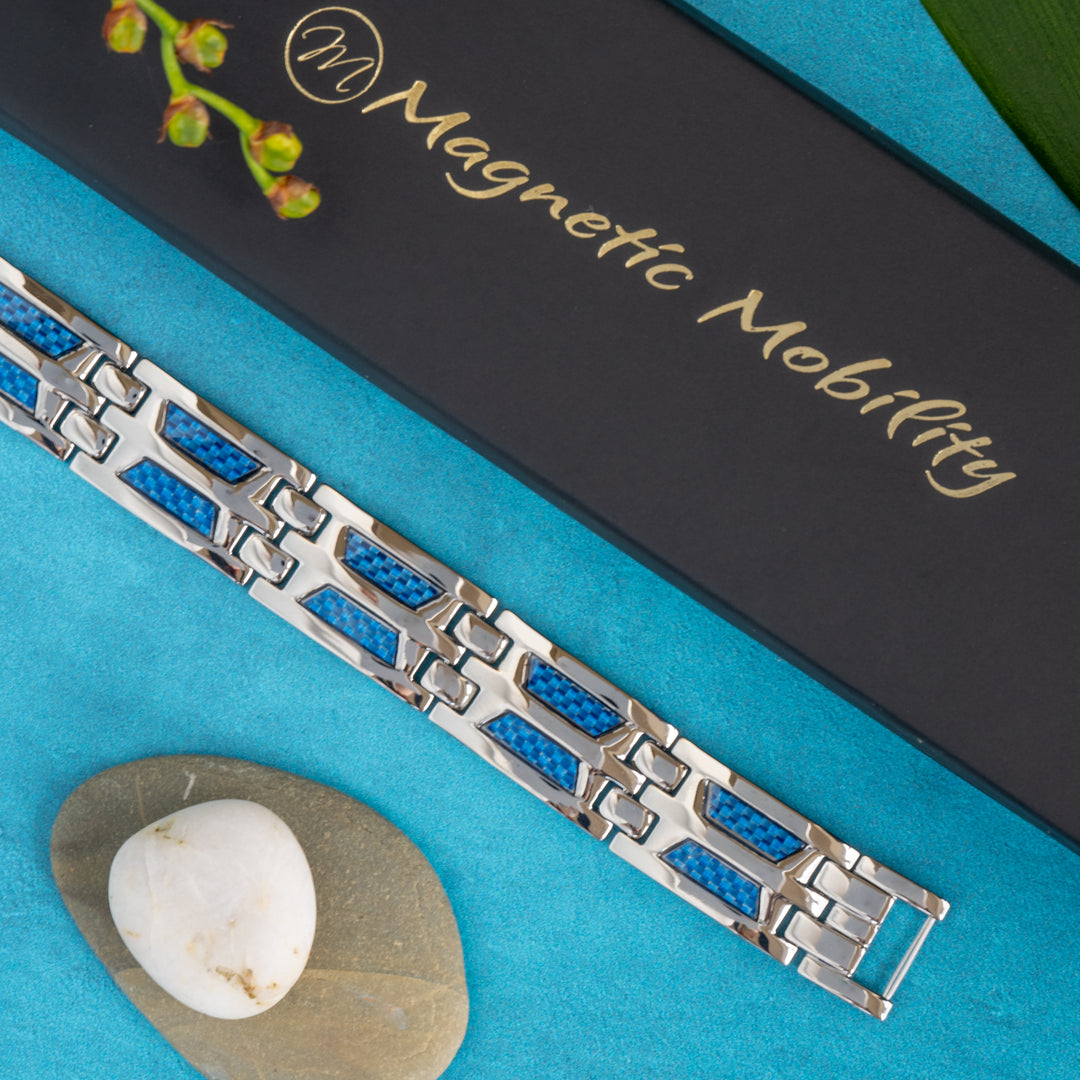 Top view of the Magnetic Mobility Yarrow Star 4in1 Magnetic Bracelet elegantly placed on a blue surface, showcasing its silver link design with vibrant blue carbon fiber inlays. The brand's sophisticated black box with gold script is partially visible, adding to the premium presentation of this health-conscious accessory, perfect for Google Shopping viewers seeking style and wellness.