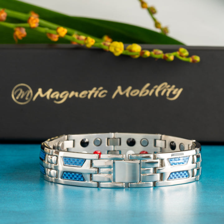 The Yarrow Star 4in1 Magnetic Bracelet by Magnetic Mobility is showcased against a vibrant blue backdrop, highlighting the bracelet's unique silver craftsmanship and blue carbon fiber details. A close-up on the secure clasp mechanism ensures confidence in wear. The brand's luxurious black box with gold logo provides a sophisticated background, adding to the product's appeal browsers interested in combining style with wellness benefits.