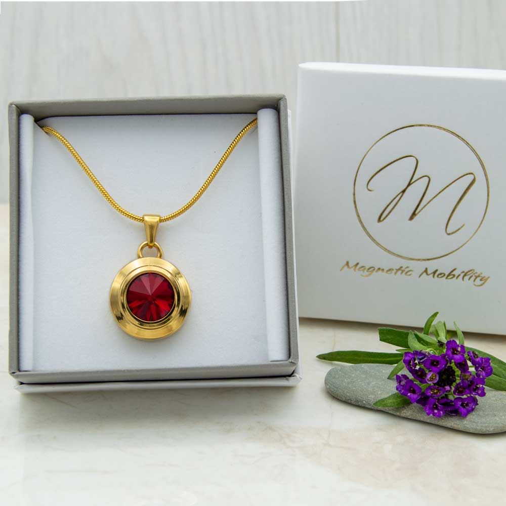 Front view of the Angelica Sun gold plated magnetic necklace with a red Swarovski stone. The necklace is in a eco-friendly gift box.