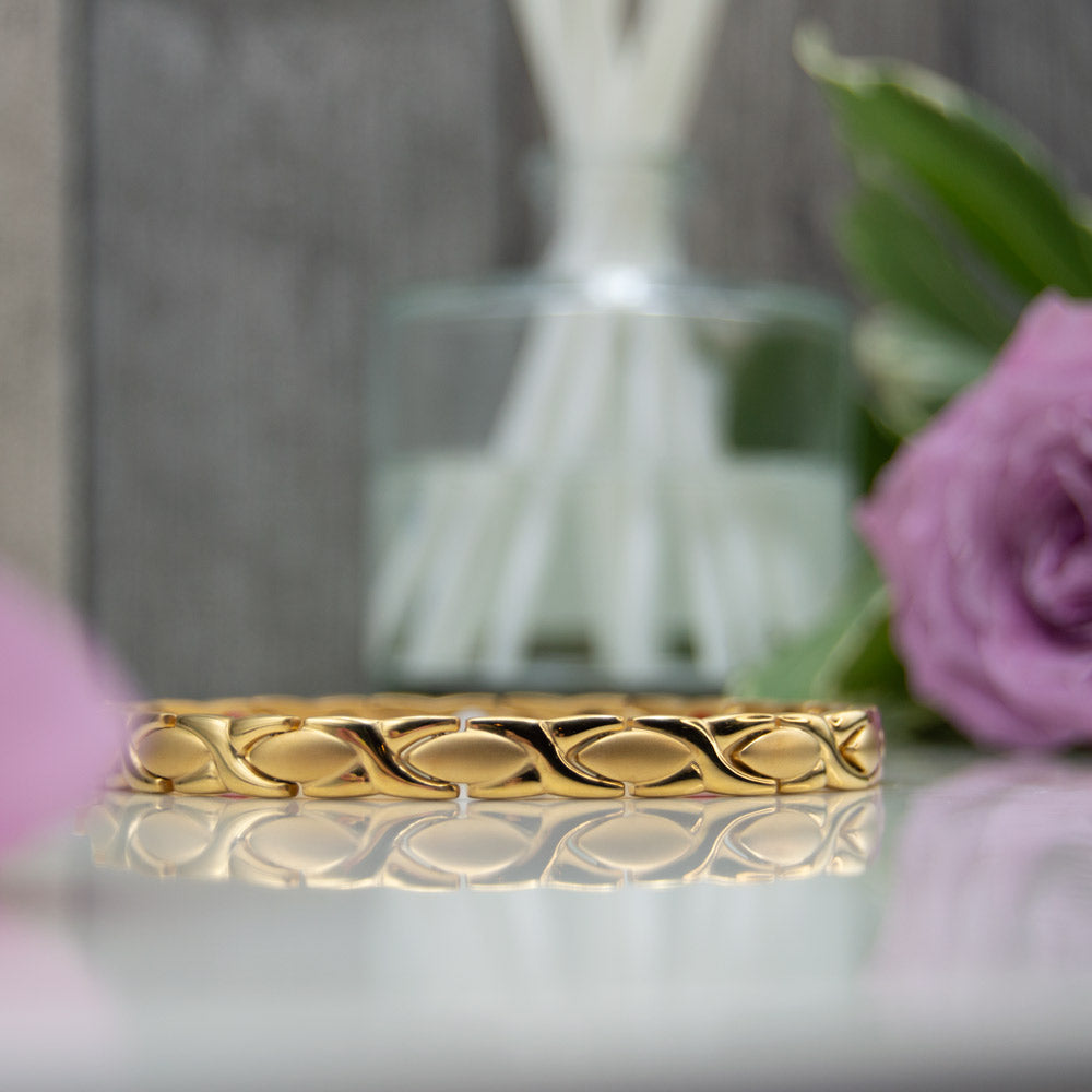 Laurel Sun - Gold 4in1 Magnetic Bracelet for Women shown on a eflective surface with pink roses