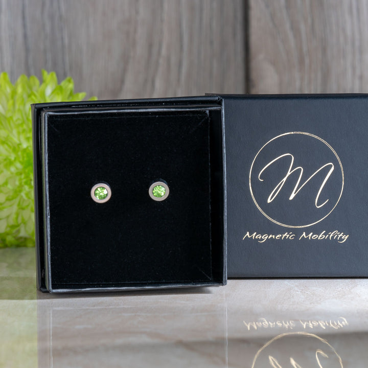 Chic August Birthstone magnetic earrings featuring brilliant Swarovski Peridot crystals, displayed in a black box with green floral accents. These earrings are designed for elegance and therapeutic benefits, perfect for August birthday gifts.