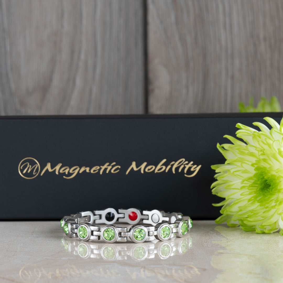 Close-up of the August Birthstone magnetic bracelet adorned with radiant Swarovski Peridot crystals, set against a black gift box with green floral elements. This bracelet combines the lush beauty of peridot with health benefits, ideal for August gifts.