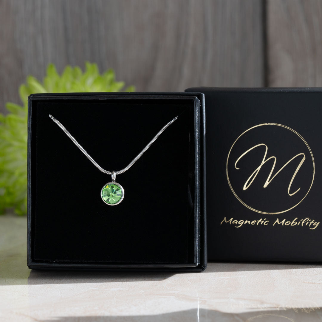 The August Birthstone magnetic necklace with a vibrant Swarovski Peridot pendant, presented in a sleek black box against a green floral backdrop. This necklace embodies the refreshing beauty of August’s birthstone, ideal for gifting or personal elegance.