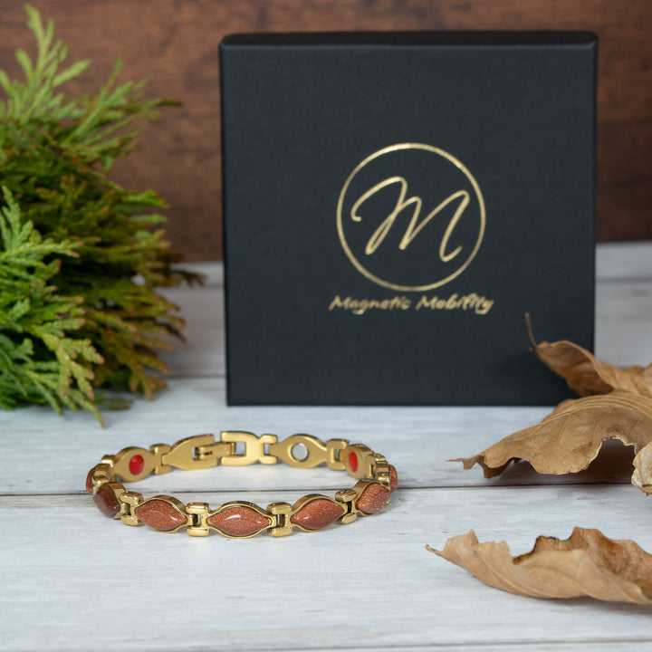 Gold magnetic bracelet with red stones on a wooden surface next to a black box with 'Magnetic Mobility' branding.