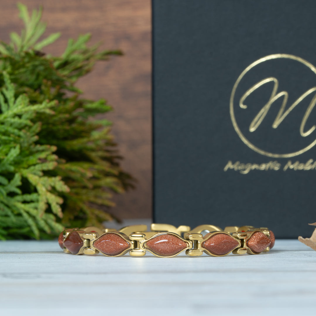 Gold bracelet with red stones on a white surface, with a branded box in the background.