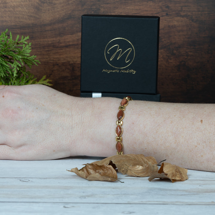 Magnetic Bracelet on a wrist with a black box and decorative leaves on a wooden surface