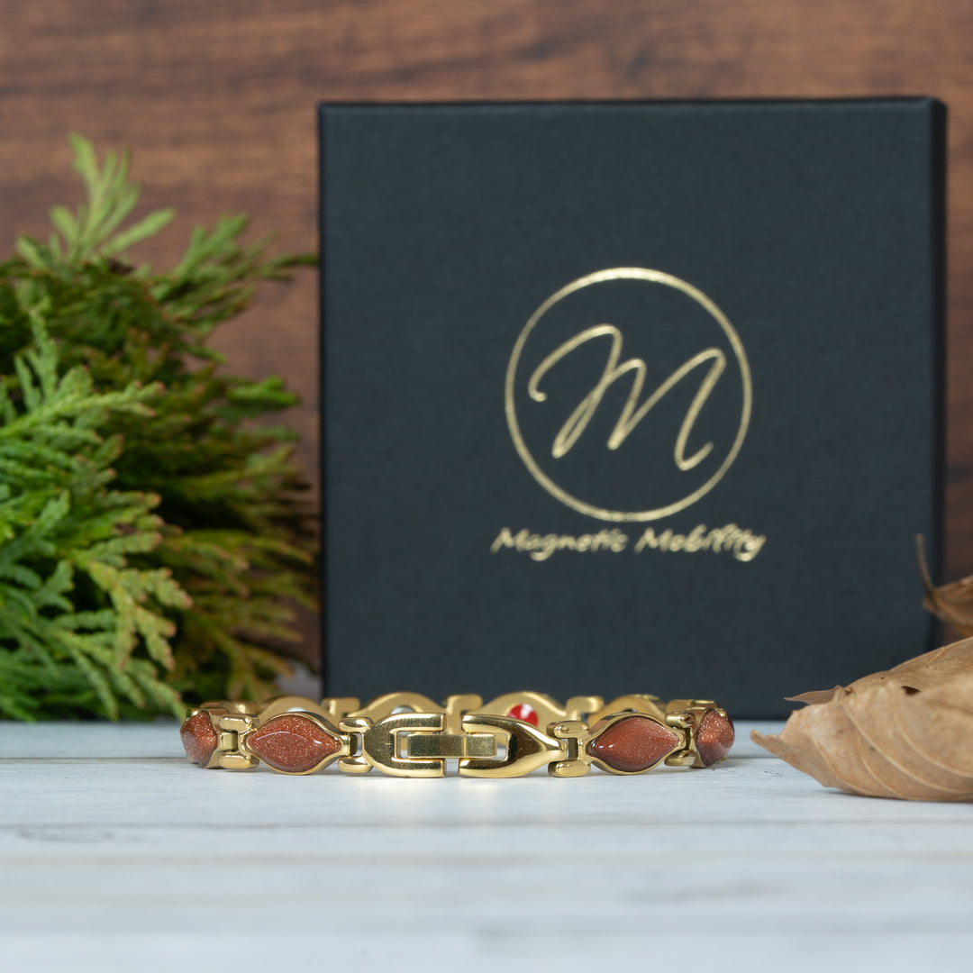 Gold bracelet with red stones in front of a black box with 'Magnetic Mobility' . Clasp viewlogo