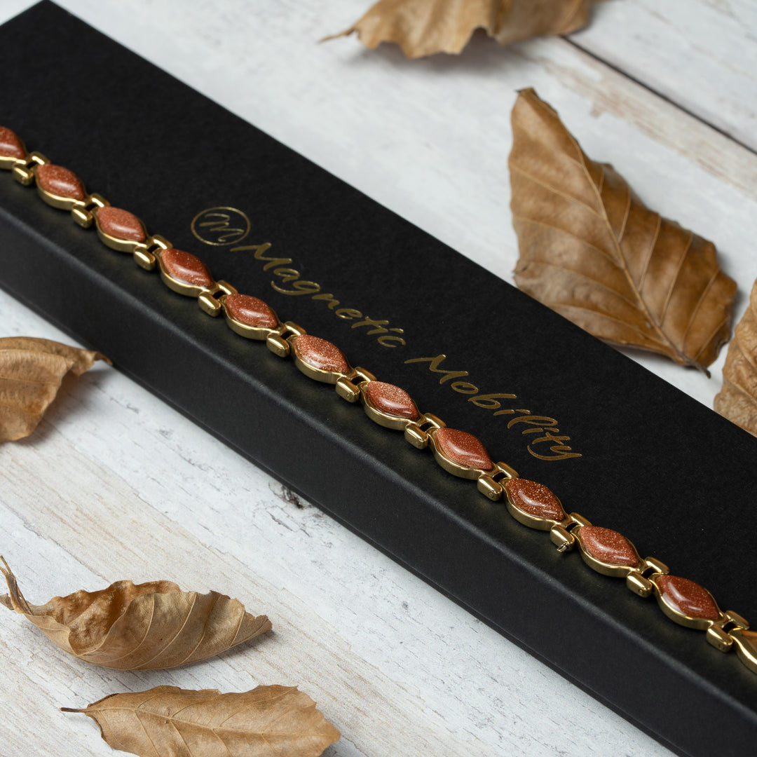 Magnetic Bracelet with red stones on a black box labeled 'Magnetic Mobility' surrounded by dried leaves.