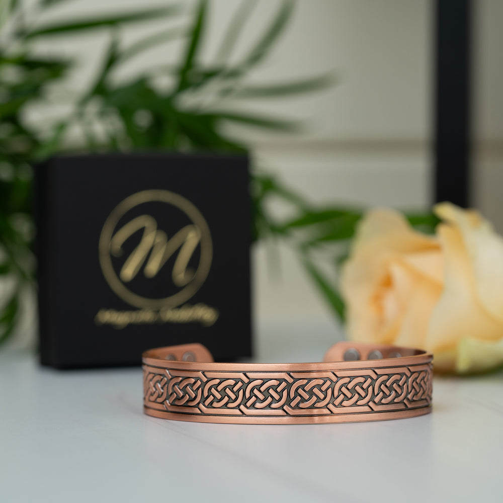 Front view of the Burdock Copper Bracelet with a detailed display of the Celtic knot design, placed next to a Magnetic Mobility branded box.