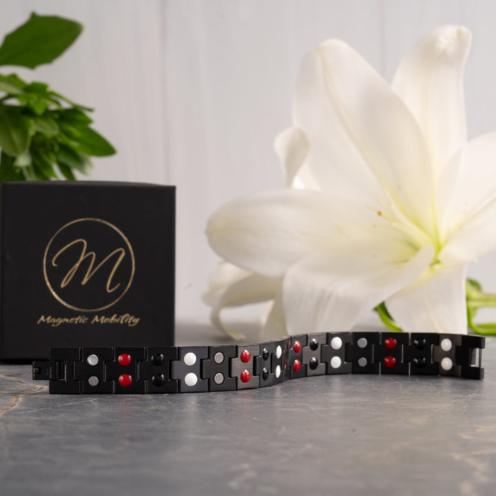 Burnet Night 4in1 Magnetic Bracelet displayed against a floral backdrop, featuring an all-black design with therapeutic elements visible on the band.