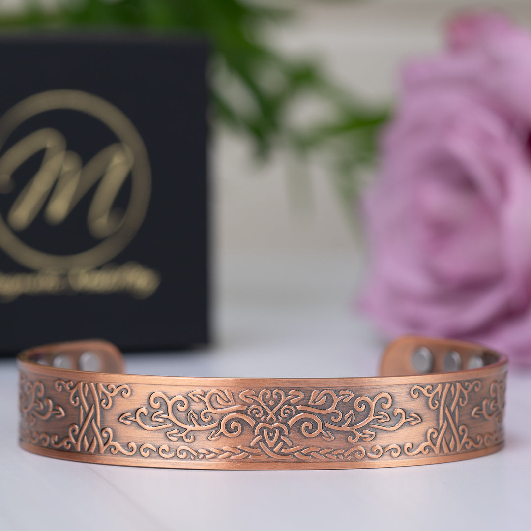 Front view of the Campion Copper Bracelet with intricate floral design, showcasing its beautiful craftsmanship. The black Magnetic Mobility box is visible in the background, complemented by a pink rose.