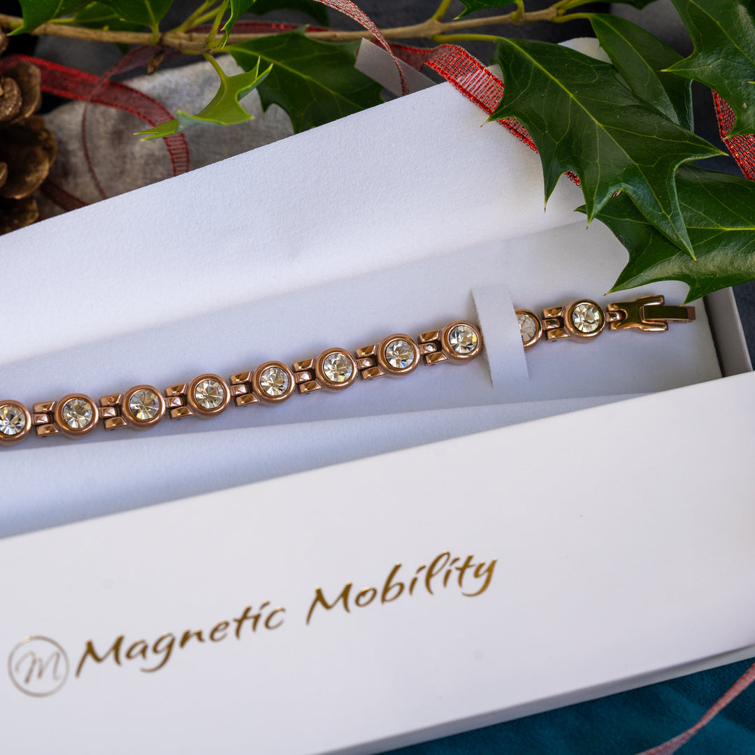 Women's Rose gold magnetic bracelet with white crystals inside an eco-friendly gift box, surrounded by Christmas decorations