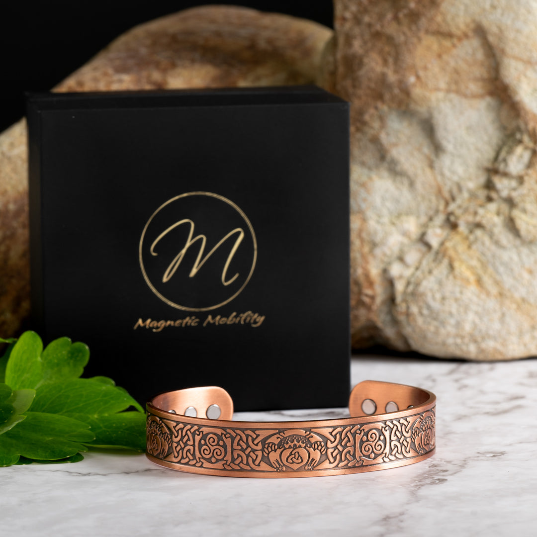View shows the Claddagh Copper Bracelet infront of a Black Eco-friendly gift box with the Magnetic Mobility Logo on it. Claddagh copper bracelet featuring a claddagh design - A crowned heart held by two hands - Symbolically, the heart represents love, the crown denotes loyalty, and the hands are a sign of friendship. Inside the heart is a triquetra symbol. The Claddagh design is surrounded by Celtic designs.
