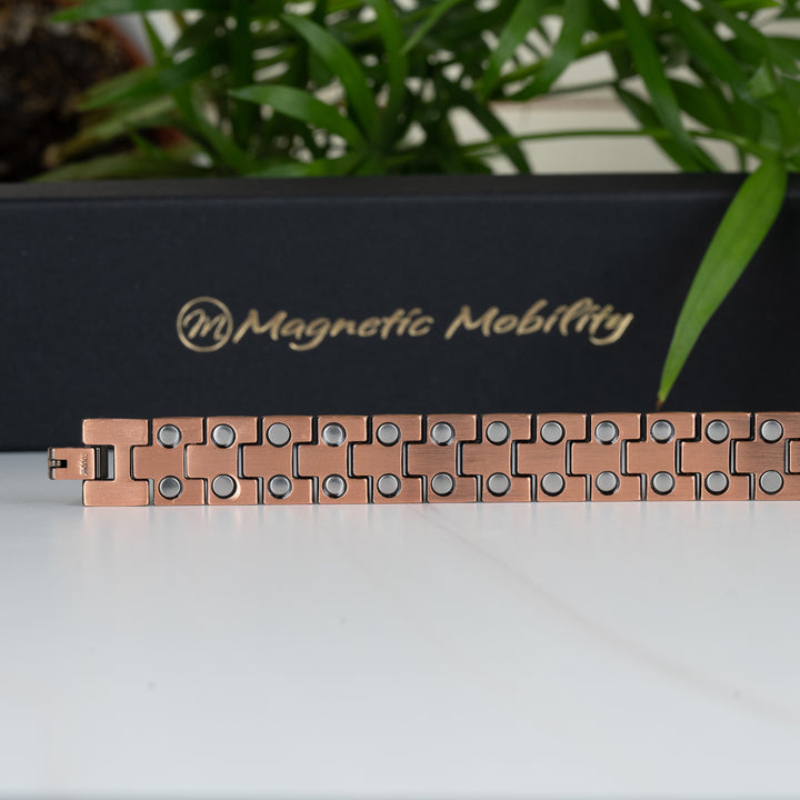 Close-up of the Columbine Copper Bracelet lying flat, showcasing the interior side with multiple double-strength neodymium magnets on each link. Black gift box with Magnetic Mobility logo in the background.