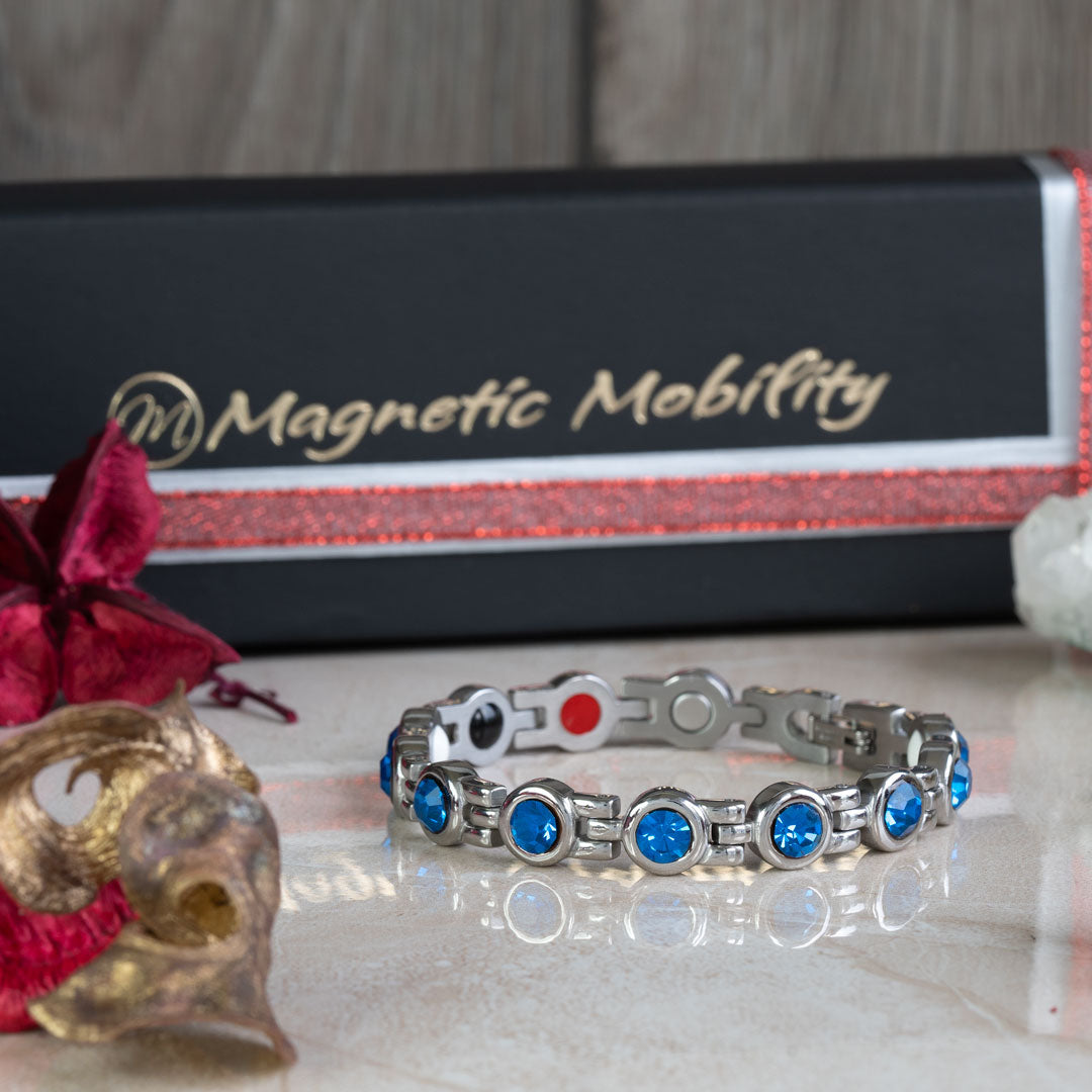 December birthstone magnetic bracelet with Swarovski Blue Zircon, displayed in a festive Christmas setting with a red ribbon and seasonal decorations, against a Magnetic Mobility branded box.