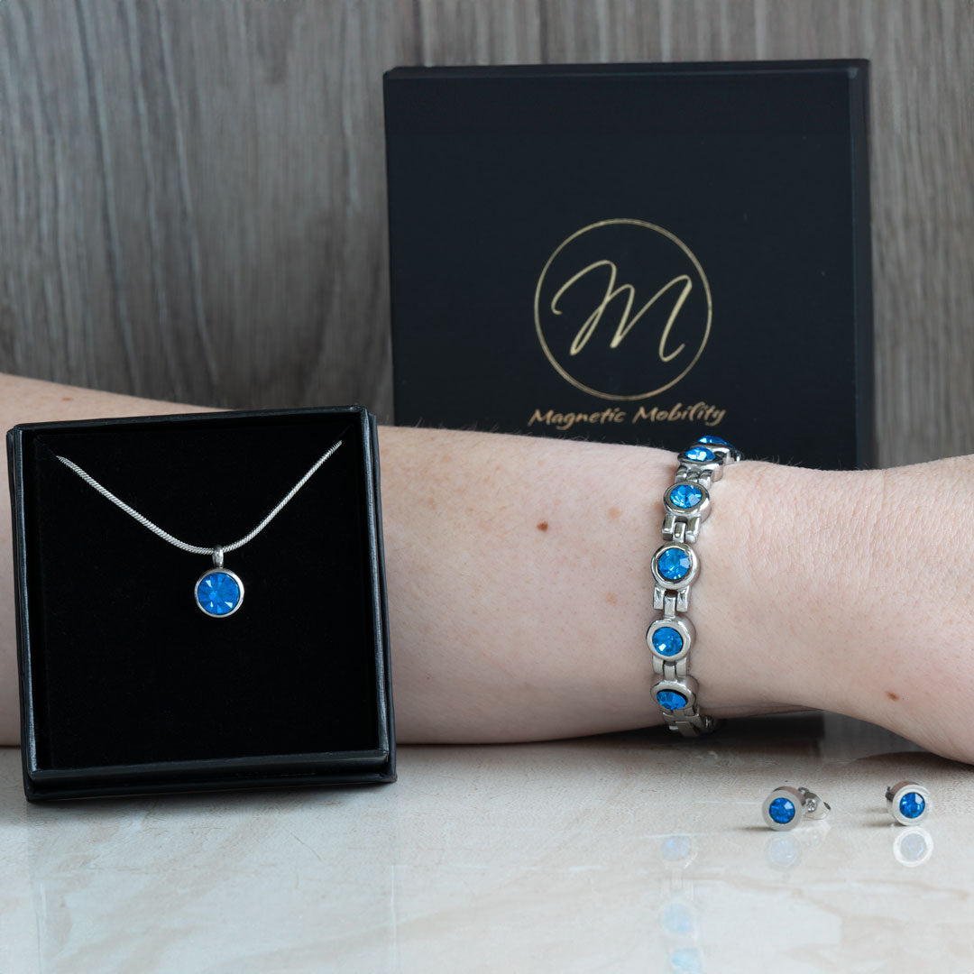 December birthstone 4in1 magnetic bracelet featuring Swarovski Blue Zircon, shown on a wrist from the front view with a focus on the vibrant blue crystals, and accompanied by pink flowers.