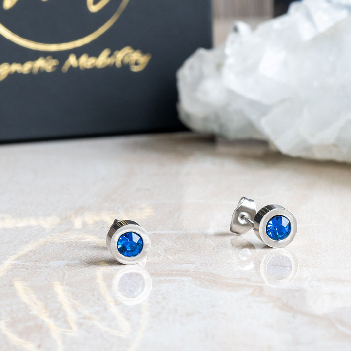 Close-up view of December birthstone magnetic earrings featuring Swarovski Blue Zircon, elegantly placed against a background of clear crystal and Magnetic Mobility packaging.