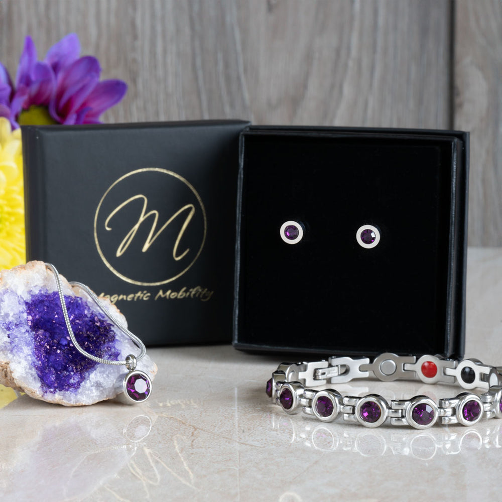 Febraury Birthstone gift set containing a 4in1 Magnetic bracelet with February birthstone Swarovski Amethyst crystals, a February birthstone necklace with one Swarovski Amethyst crystal and a neo-dynimum magnet in the back and a pair of February Birthstone magnetic earrings with Neodynimum magnets in the back. Shown in a black luxury gift box and the necklace on a amethyst geode