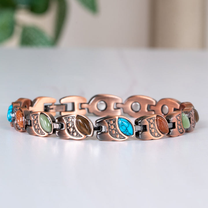 Bracelet with colorful stones on a white surface with a blurred green plant in the background