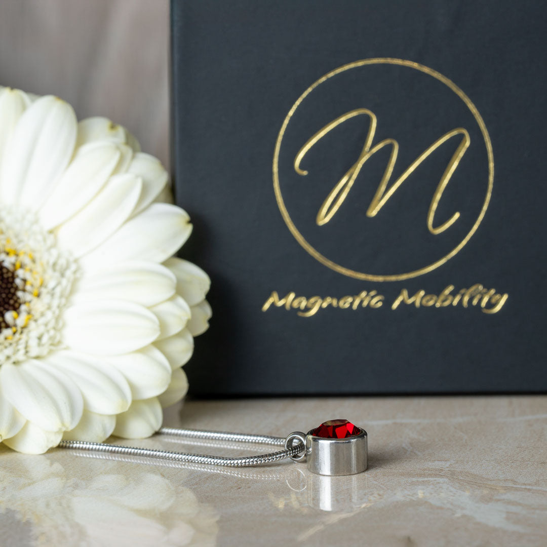 Close-up view of the July Birthstone magnetic necklace featuring a stunning Swarovski Ruby pendant, laid out elegantly with a white flower and black gift box as a backdrop. Perfect for adding a touch of elegance to July birthdays.