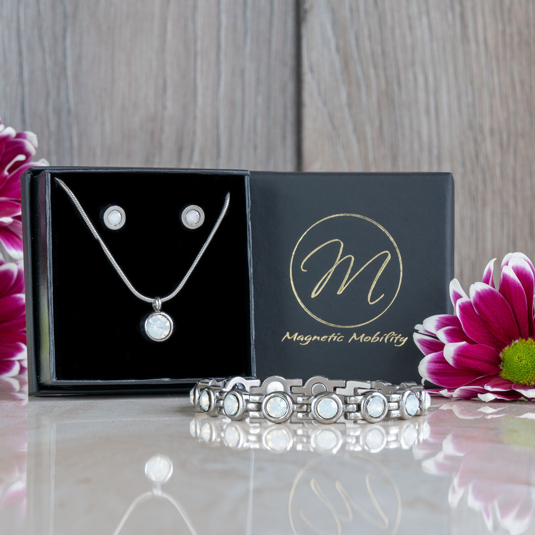 he complete June Birthstone magnetic gift set, featuring a bracelet, necklace, and earrings with Swarovski Pearls, displayed against a luxurious packaging and surrounded by pink flowers. Ideal for those looking for elegant and health-enhancing June birthstone gifts.