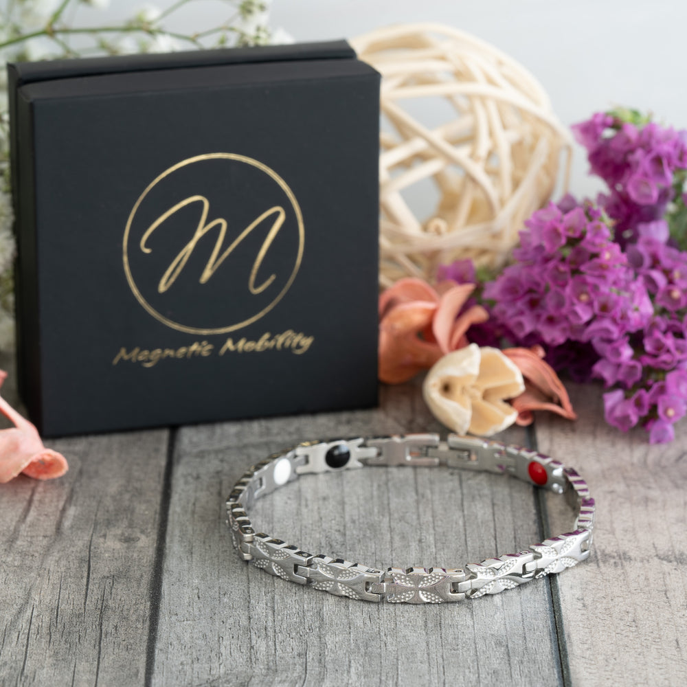 Meadowsweet Star 4in1 Magnetic Bracelet by Magnetic Mobility, featuring a silver butterfly design. This elegant bracelet offers four therapeutic elements: Neodymium magnets, FIR (Far Infrared) elements, Germanium, and Negative Ions. Perfect for arthritis relief and joint pain support. Shown in a stylish 45-degree view with a luxurious gift box and floral accents.