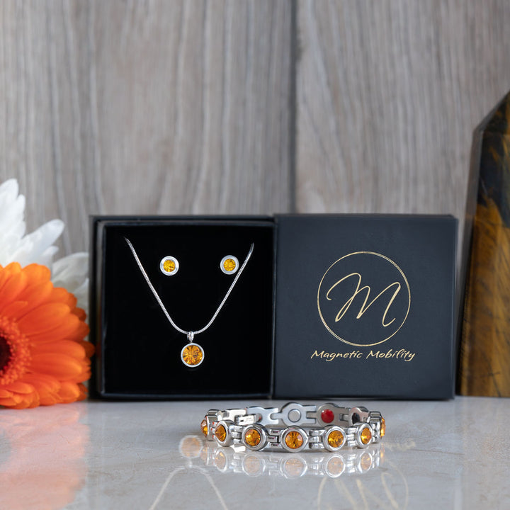 Close-up of the November birthstone necklace and earrings set, featuring bright citrine stones. The jewelry is elegantly displayed in a black box with an orange flower nearby, emphasizing the citrine's vibrant color and the Magnetic Mobility logo on the box.