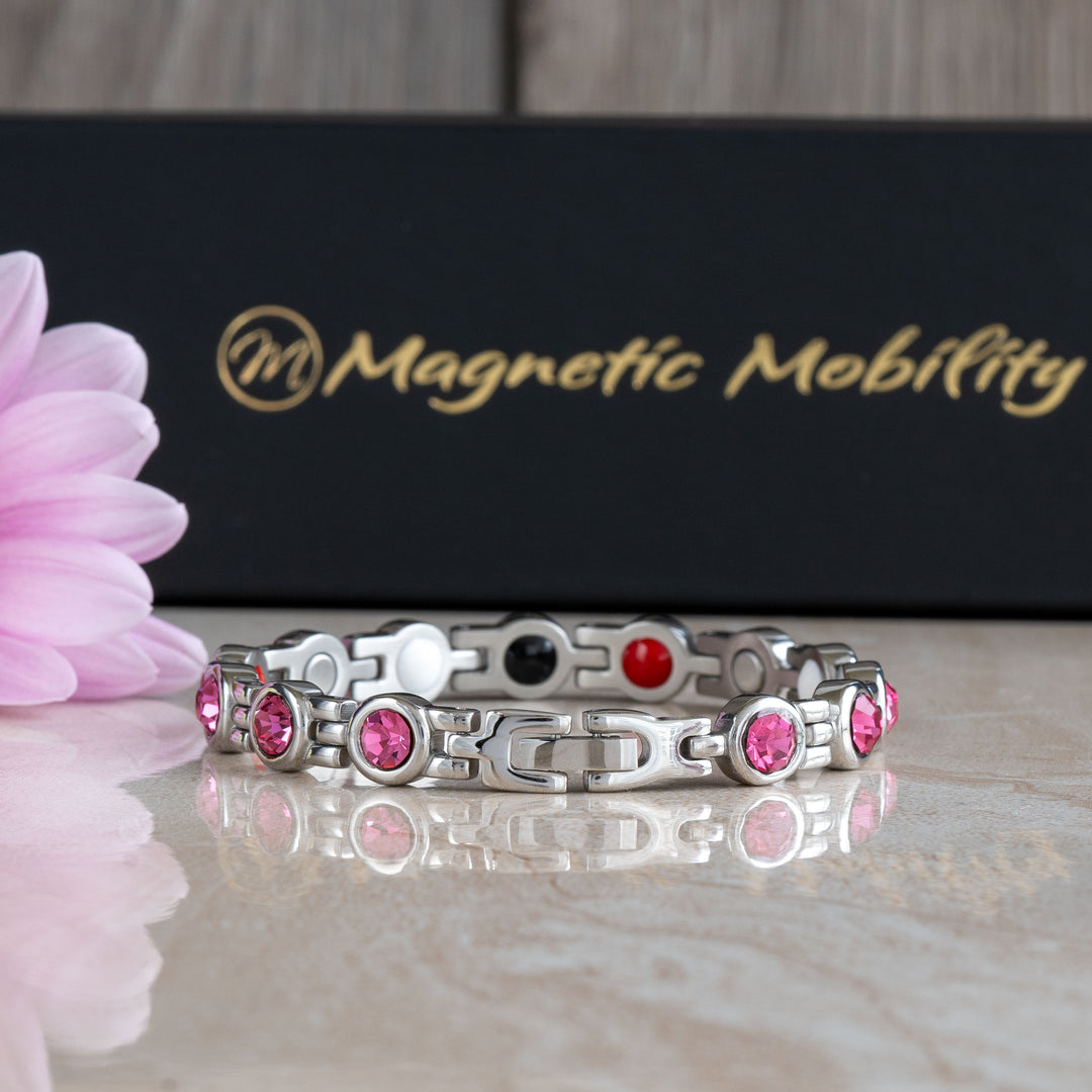 Close-up detail of the clasp of a pink tourmaline magnetic bracelet from Magnetic Mobility. The bracelet’s intricate design and pink crystals are highlighted, with a pink flower and brand packaging in the background.