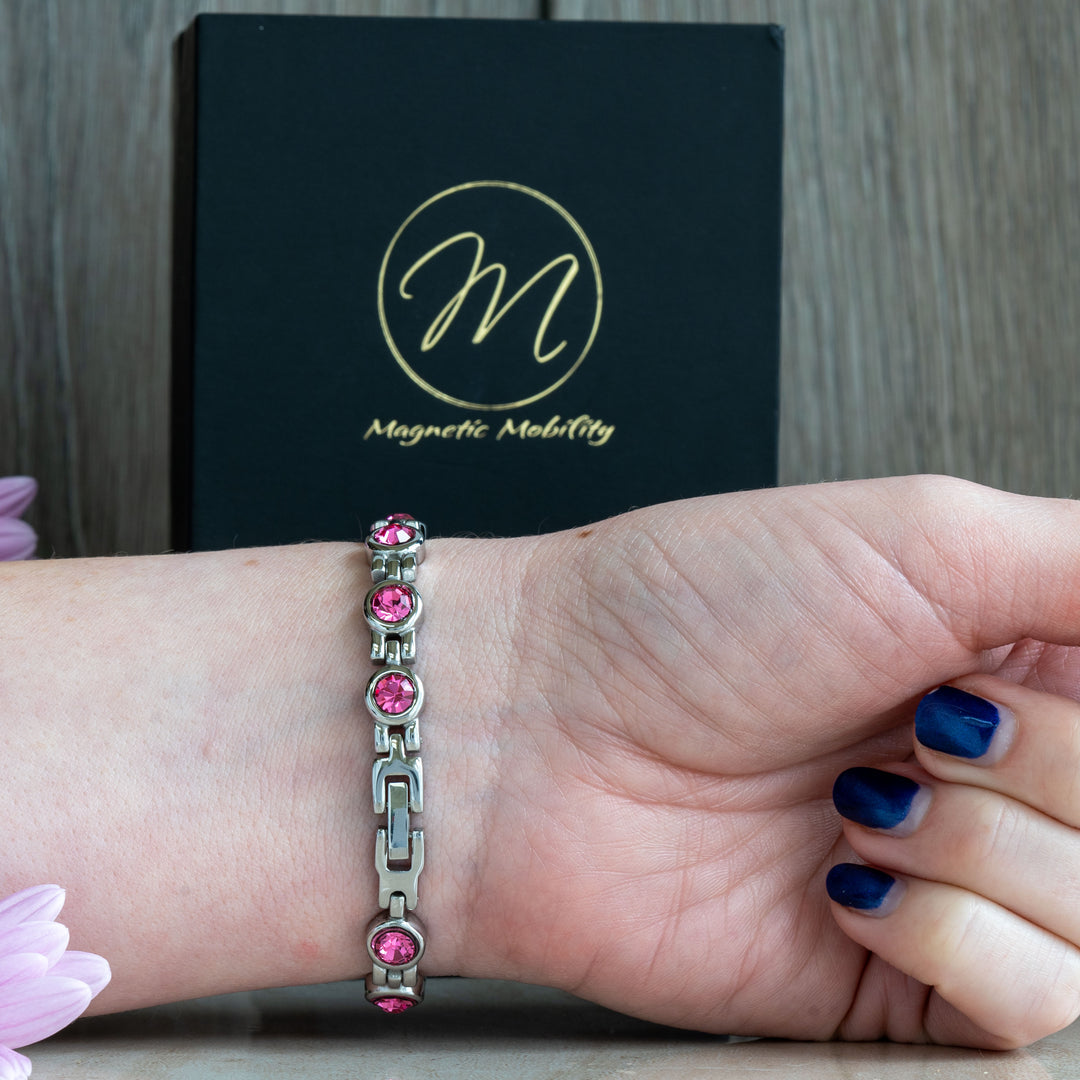 Clasp view of a pink tourmaline magnetic bracelet from Magnetic Mobility, showcasing the secure and stylish clasp mechanism. The bracelet is adorned with pink crystals and is worn on a woman’s wrist, with the brand’s packaging visible in the background.