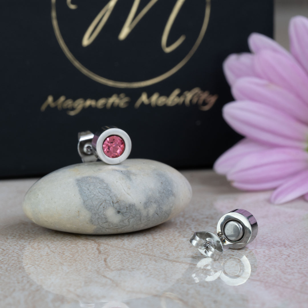 Back view of pink tourmaline magnetic stud earrings from Magnetic Mobility, showing the secure magnetic backing and sleek silver setting. The earrings are placed beside pink flowers and the brand’s black packaging.