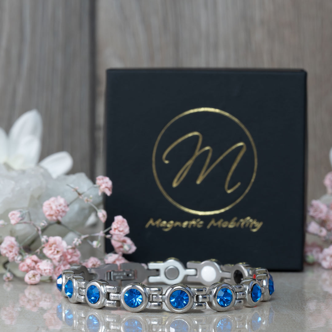 Close-up of the September Birthstone magnetic bracelet adorned with radiant Swarovski Blue Sapphire crystals, displayed against a black gift box with pink flowers. This bracelet combines the deep beauty of sapphires with health benefits, perfect for September gifts.