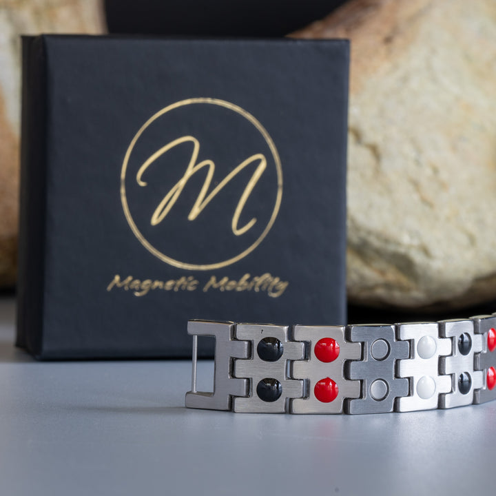 Magnetic Mobility bracelet displaying a double row of red and black therapeutic elements on the reverse side, placed beside a branded black box, against a stone background.