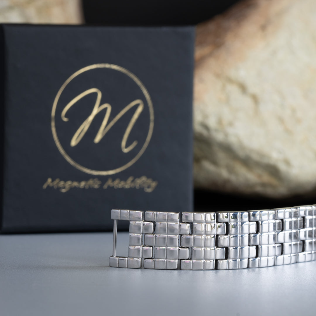 Magnetic Mobility's silver arthritis relief bracelet with a distinctive linked design, placed next to a branded black box, set against a stone backdrop