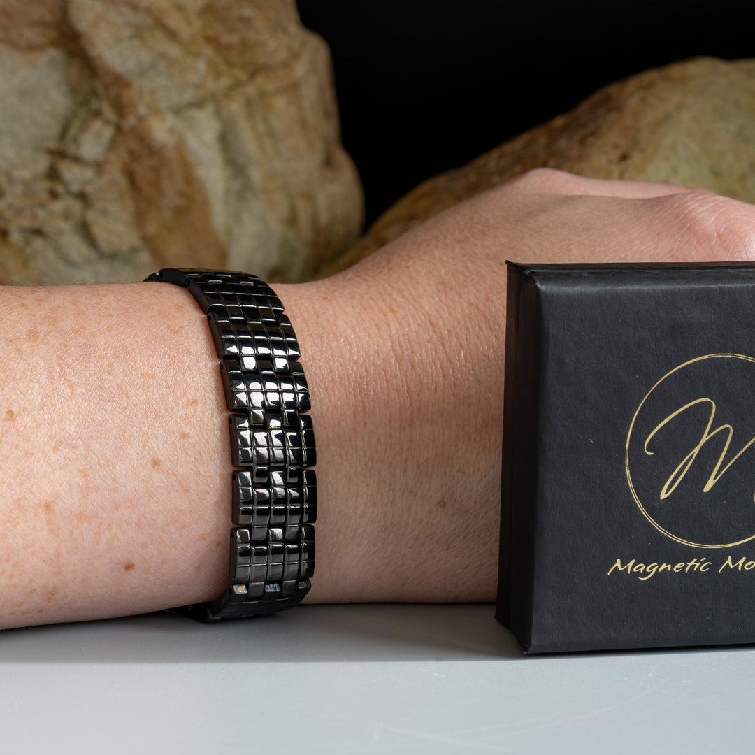 Wearer showcasing Magnetic Mobility's Double Row Magnetic Bracelet on wrist, accompanied by Signature Logo Box and set against a natural stone backdrop.