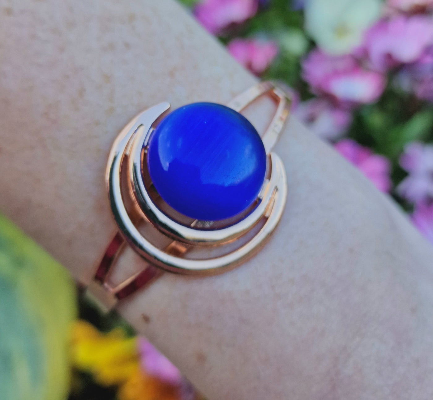 A woman's wrist adorned with the Orchid Moon Women's Copper Bracelet. The elegant copper bracelet features a captivating crescent moon design with a dark blue stone, exuding charm and style. Its therapeutic magnets discreetly embedded on the back offer potential relief for arthritis and back pain. Experience the perfect blend of fashion and function with this exquisite accessory on a woman's wrist.