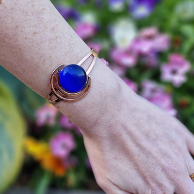 Version 2 of  A woman's wrist adorned with the Orchid Moon Women's Copper Bracelet. The elegant copper bracelet features a captivating crescent moon design with a dark blue stone, exuding charm and style. Its therapeutic magnets discreetly embedded on the back offer potential relief for arthritis and back pain. Experience the perfect blend of fashion and function with this exquisite accessory on a woman's wrist.