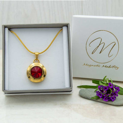 Front view of the Angelica Sun gold plated magnetic necklace with a red Swarovski stone. The necklace is in a eco-friendly gift box. 