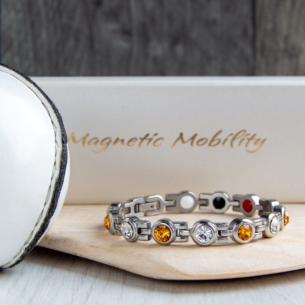 Armagh County GAA Inspired Women's Magnetic Bracelet displayed on a hurl. A stylish blend of county colours and magnetic therapy benefits, offering relief from migraines, sports injuries, fibromyalgia, and more. Perfect for any GAA fan and daily wear.