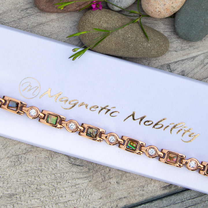 Rose Gold Magnetic Bracelet for Women with Irredessant designs and White crystals. Image shows the bracelet on a white luxury gift box for jewellery. 