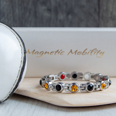 Kilkenny County GAA Inspired Women's Magnetic Bracelet resting on a hurl. Blending county colours with magnetic therapy benefits, aiding in the relief from migraines, sports injuries, and more